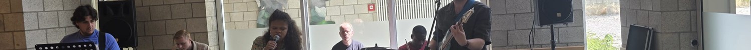Blind Vision Band, bestehend aus drei Schülern, einer Schülerin und zwei Lehrkräften, steht im Foyer und singt sowie spielt verschiedene Instrumente