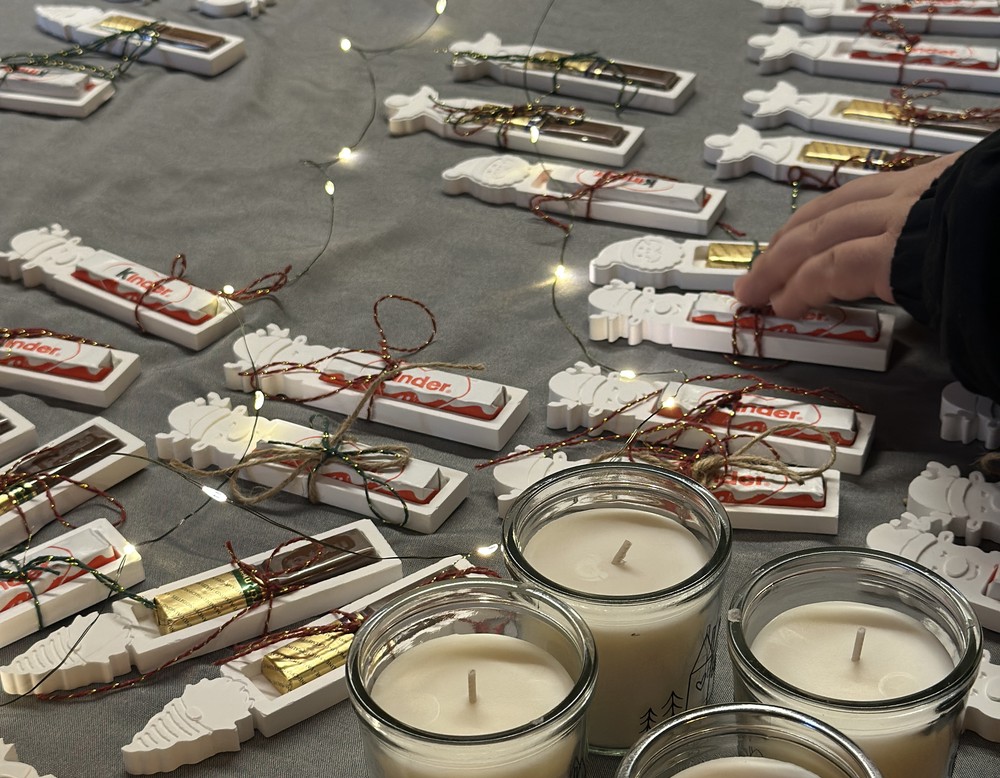 Kerzen sowie Merci- und Kinderschokolade in einem weihnachtlich dekorierten Holzrahmen.