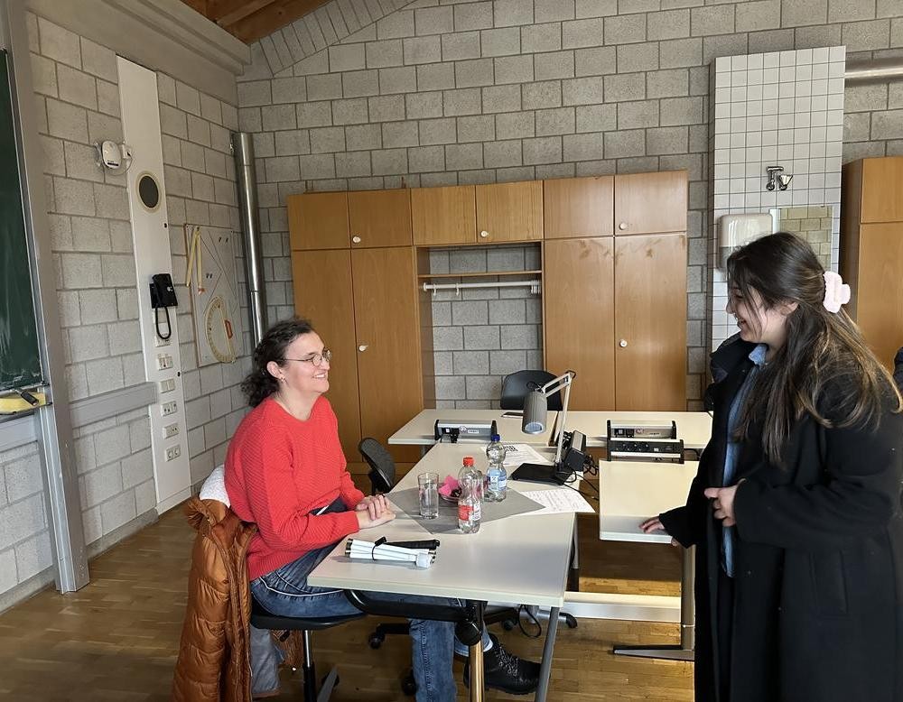 Die Referendarin sitzt, und eine Schülerin steht vor ihr.