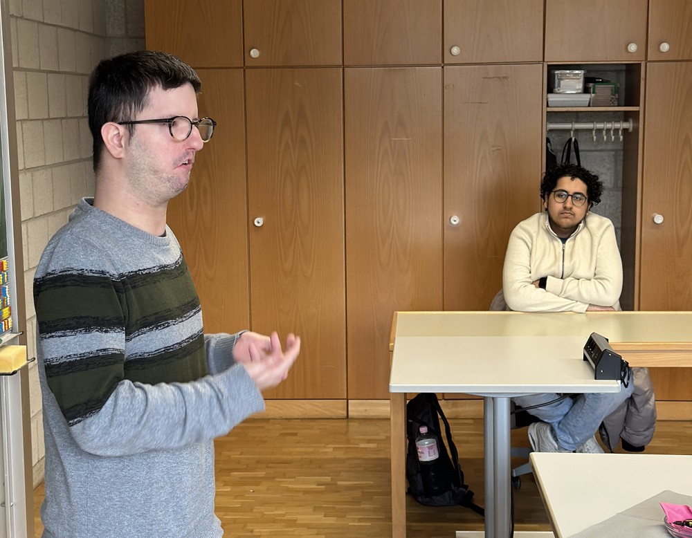 Der Referent spricht und begleitet seine Ausführungen mit einer dezenten Handbewegung. Ein Schüler sitzt rechts von ihm und hört zu