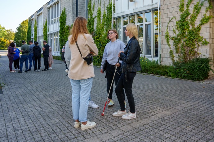 Schüler und Schülerinnen sowie Lehrer und Lehrerinnen stehen auf dem Schulhof und führen Gespräche.
