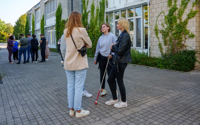 Schüler und Schülerinnen sowie Lehrer und Lehrerinnen stehen auf dem Schulhof und führen Gespräche.