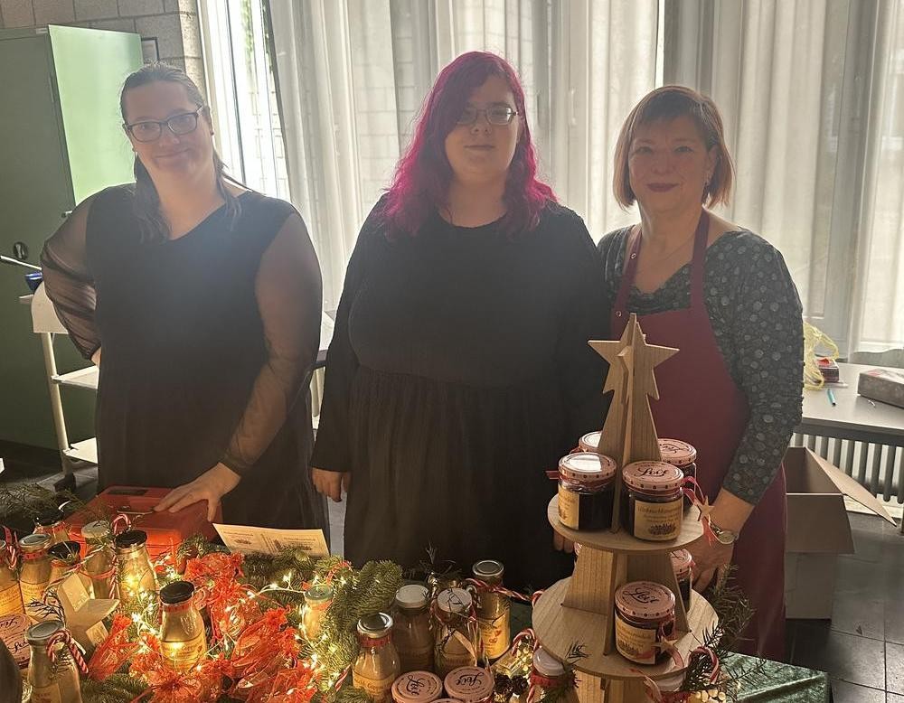 Schülerinnen, Schüler und Lehrkräfte hinter dem Verkaufsstand mit dem von der BFE hergestellten Badesalz, Weihnachtscappuccino und Marmelade.