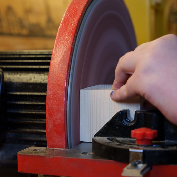 Schülerin schleift Holz an der Schleifmaschine (vergrößerte Bildansicht wird geöffnet)