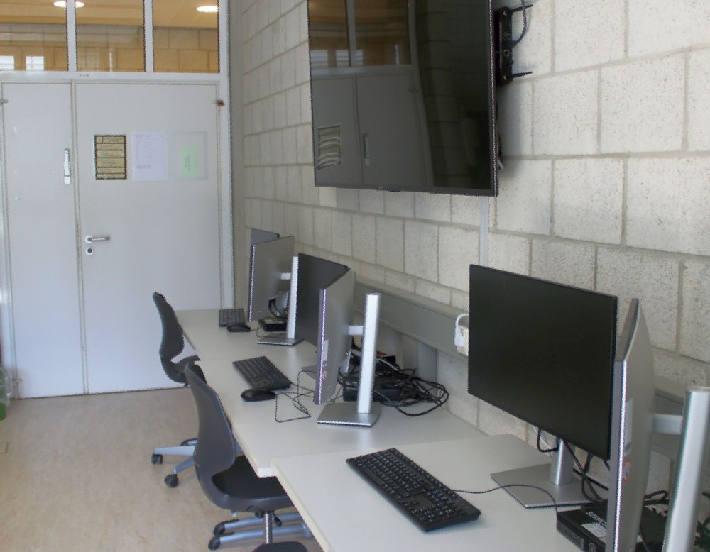 Arbeitsplatz mit 2 Bildschirmen und einen großen Fernseher an der Wand