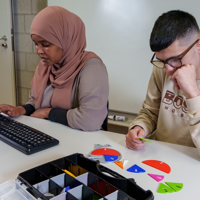 Eine Schülerin arbeitet am PC, während ein Schüler die Bruchrechnung mit Teilen aus dem 3D-Drucker übt. (vergrößerte Bildansicht wird geöffnet)