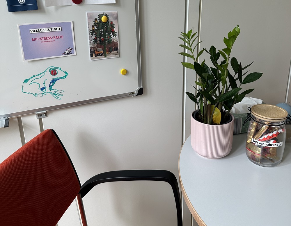 Ein roter Stuhl und ein Schreibtisch mit Blumen, Nervennahrung und Taschentüchern.