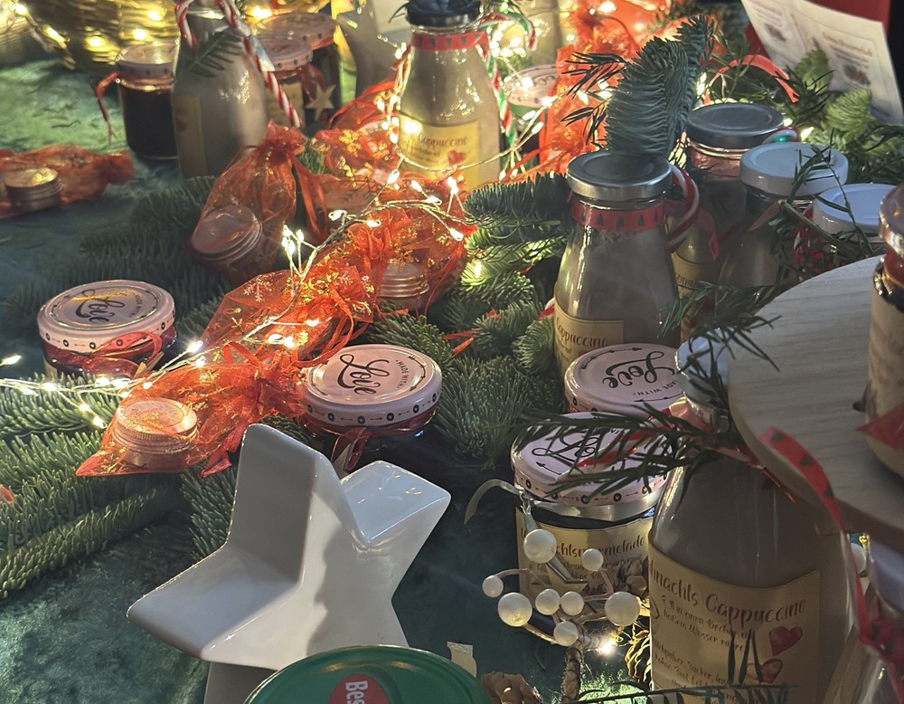 Auf einem weihnachtlich dekorierten Tisch mit Lichterketten, Weihnachtssternen und Tannenzapfen stehen Marmelade und Weihnachtscappuccino.