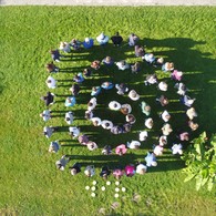 Menschenspirale aus Lehrern und Lehrerinnen sowie Schülern und Schülerinnen mit der Unterschrift „Wir“.